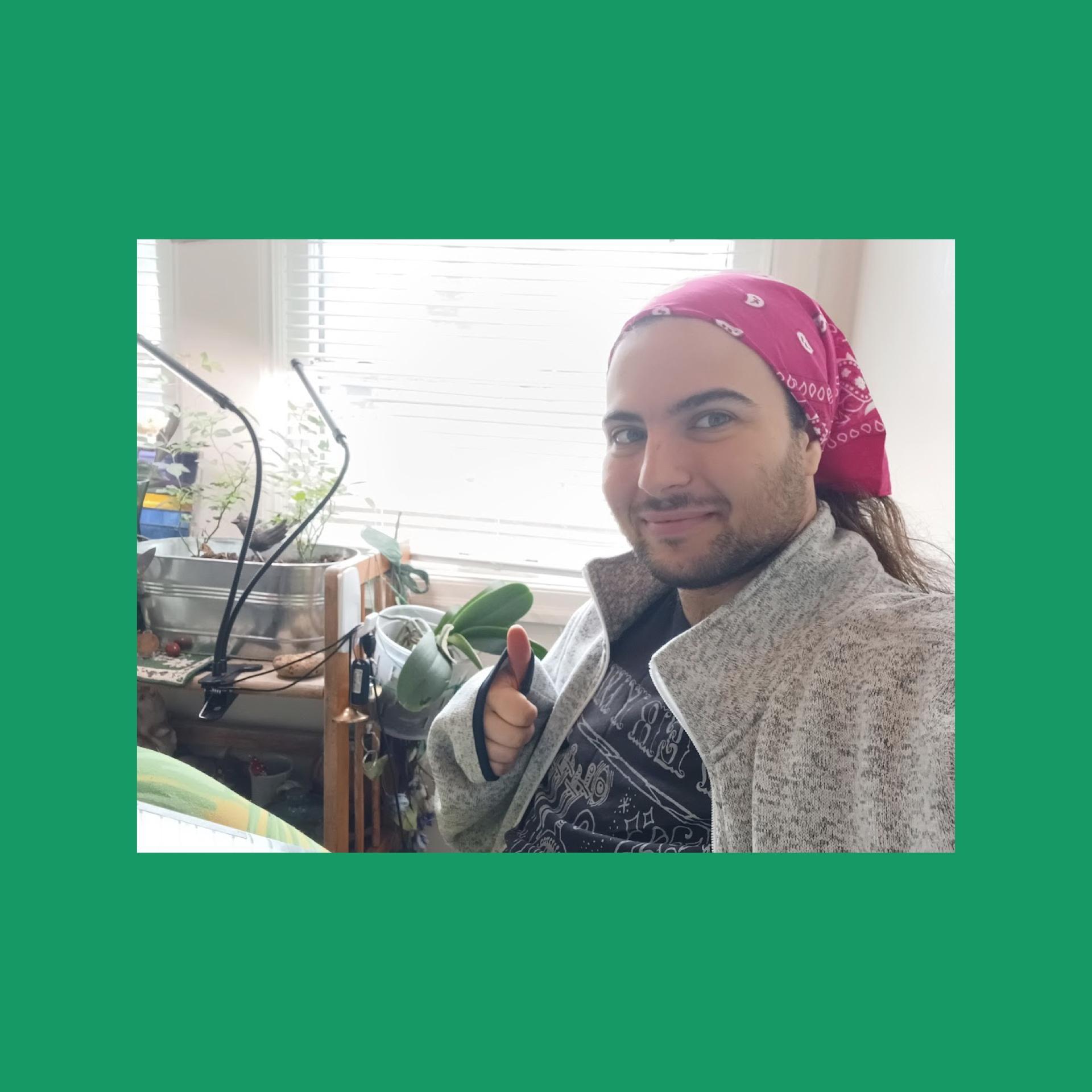 A graduate researcher wearing a bandana and holding up a thumbs up sign looks at the camera